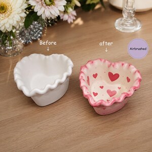 May include: Two heart-shaped ceramic bowls with ruffled edges. The left bowl is plain white, labeled "Before". The right bowl is airbrushed with pink edges and small red heart patterns on the interior, labeled "after" and "Airbrushed".