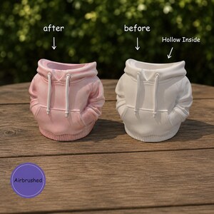 May include: Two hoodie-shaped planters, one light pink and one white, each featuring a hood, drawstrings, and a front pocket. Text labels include after, before, Hollow Inside, and Airbrushed. The planters have a hollow interior.