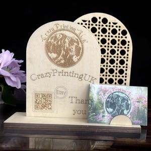 May include: A wooden business card holder with a laser-engraved design. The design features a dog, the text "Crazy Printing UK", and a QR code. The holder has a slot for a business card and a lattice design on the side.