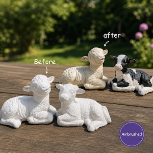 May include: Four animal figurines are displayed. Two are plain white lambs, one is a textured beige lamb labeled 'Before' and 'after', and one is a black and white calf labeled 'Airbrushed'. The figurines are in a reclining position.