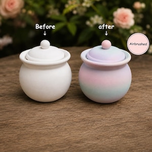 May include: Two small round lidded jars. The left jar is solid white with a matching lid and knob. The right jar features a pastel gradient of pink, blue, and purple with a pink knob. Text labels read Before, after, and Airbrushed.
