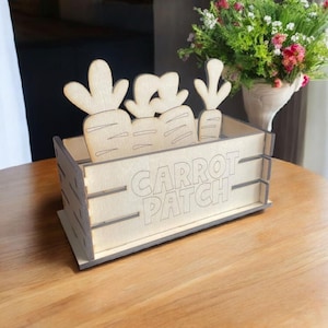 May include: Wooden crate with a carrot patch design. The crate is made of light wood and has a cutout of carrots on the front. The crate is labeled "Carrot Patch".