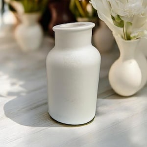 May include: A white ceramic vase with a textured surface. The vase is round and has a wide opening at the top.