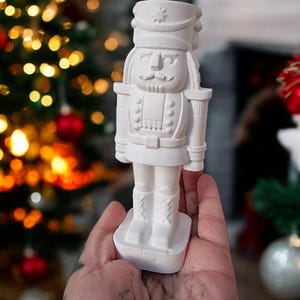 May include: White ceramic nutcracker figurine with a painted face and a star on its hat. The figurine is standing on a base and has a detailed design.