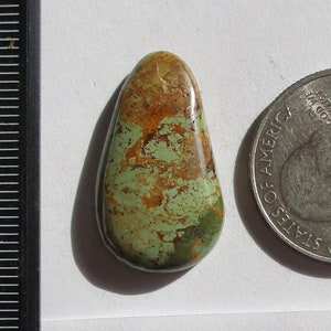 Puede incluir: Un cabujón de piedra natural de color verde, marrón y blanco, que mide 17,2 quilates, con el texto "100% Natural Rising Phoenix 1ET-66-RP 17.2ct." en una etiqueta blanca junto a una moneda de 25 centavos de dólar estadounidense.
