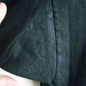 May include: Close-up of a black fabric with a subtle texture. The fabric has a slight sheen and appears to be slightly worn.