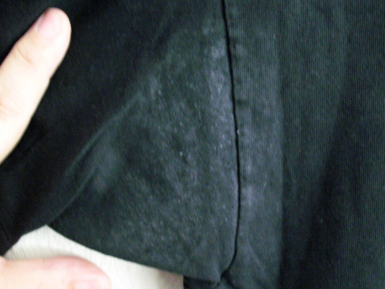 May include: Close-up of a black fabric with a subtle texture. The fabric has a slight sheen and appears to be slightly worn.
