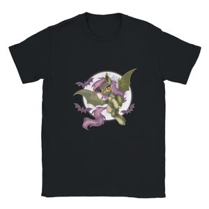 May include: A black t-shirt featuring a graphic print of a winged pony with a light green body, purple mane and tail, and orange eyes. The pony is positioned in front of a large white moon, surrounded by several small purple bats in flight.