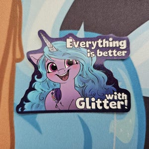 May include: A sticker featuring a cartoon pony with blue hair and a unicorn horn. The pony is purple with pink eyes and a necklace. Text on the sticker reads "Everything is better with Glitter!"