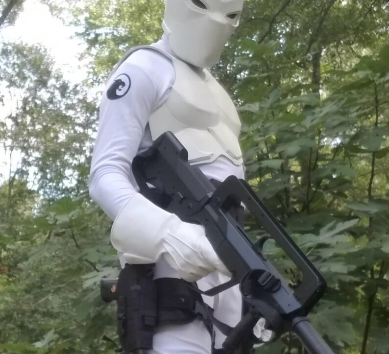 May include: A person wearing a white suit and a white helmet with a black symbol on the left arm, holding a black rifle with a scope.