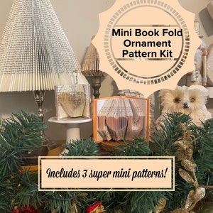 May include: A close-up of a craft kit for making mini book fold ornaments. The kit includes three patterns, as indicated by the text "Includes 3 super mini patterns!" The image shows a variety of book fold ornaments, including a heart, a bird, and a tree. The ornaments are displayed on a table with a festive background.