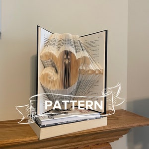 Peut inclure: Une sculpture d'art de livre représentant le chiffre 35, pliée à partir des pages d'un livre. La sculpture est exposée sur une étagère avec d'autres livres. Le mot "PATTERN" est écrit sur une bannière au-dessus de la sculpture.