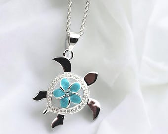 May include: Silver necklace featuring a turquoise flower pendant shaped like a turtle. The flower has a white centre and is surrounded by clear rhinestones.