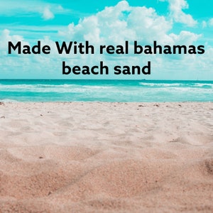 May include: A close-up of white sand on a beach with blue water in the background. The text "Made With real bahamas beach sand" is superimposed on the image.