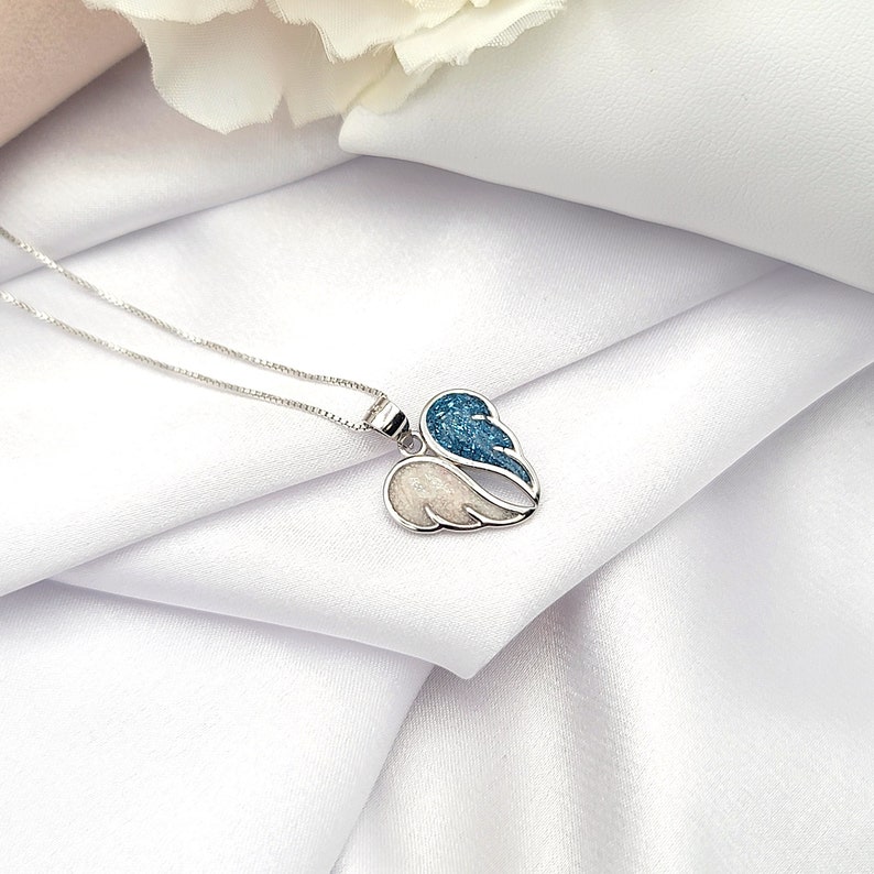 May include: A silver necklace with a heart-shaped pendant featuring two wings. One wing is blue with white glitter, and the other is white with blue glitter.
