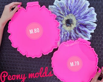 Può includere: Due stampi in silicone rosa a forma di peonie. Gli stampi sono etichettati con M.80 e M.79. Gli stampi sono su una superficie con un motivo bianco e nero.