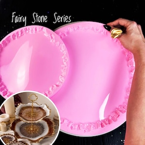 May include: Two pink silicone molds for resin casting. The molds have a scalloped edge and are designed to create a two-tiered serving tray. The molds are labeled "Fairy Stone Series".