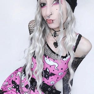 May include: A black beanie with the white text WEIRDO, a pink sleeveless dress featuring a pattern of white ghosts, black bats, and eyeballs, a black fishnet long-sleeve top, a black belt with silver grommets, and a silver chain accessory.