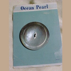 May include: A single, round, gray, mother-of-pearl button with a white center hole. The button is on a blue card with the text "Ocean Pearl" printed in blue.