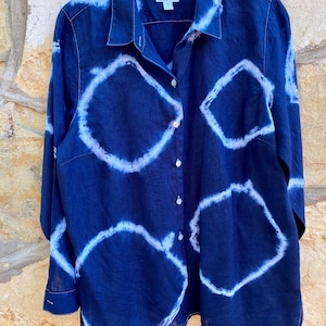 May include: A navy blue long-sleeved button-down shirt with a white tie-dye pattern. The shirt has a collared neckline and a button closure.
