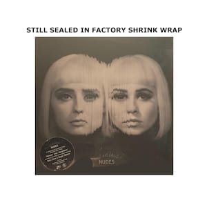 May include: A monochrome album cover showing two women with blonde wigs. The album is titled "Nudes" by Lucius. The cover is still sealed in factory shrink wrap. The album includes songs "Woman" and "Neighbors".