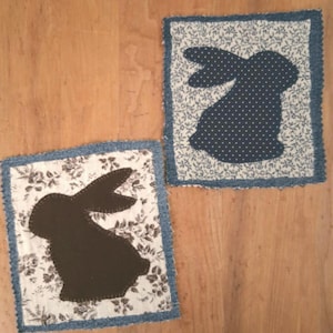 May include: Two rectangular fabric patches with frayed denim borders. One patch features a dark brown rabbit silhouette on a white floral background. The other patch displays a navy blue rabbit silhouette with white polka dots on a white floral background.