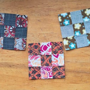 Peut inclure: Trois dessous de verre carrés en tissu disposés en groupe. Le dessous de verre de gauche présente un motif géométrique rouge, noir et blanc. Celui de droite affiche un fond marron avec des fleurs bleues et jaunes. Celui du bas a un imprimé floral.