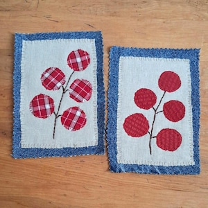Peut inclure: Deux appliqués en tissu rectangulaires avec un panneau central beige et une bordure en jean bleu foncé. Chaque appliqué présente une tige brune brodée avec cinq feuilles circulaires rouges, l'une à motif écossais et l'autre texturée.
