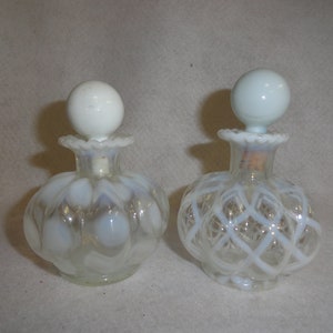 May include: Two clear glass perfume bottles with opalescent white glass stoppers. The left bottle features a rounded, ribbed body, while the right bottle displays a raised white lattice pattern. Both have ruffled rims and spherical tops.