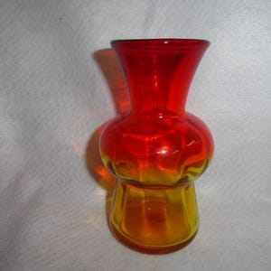 May include: A small, red and orange glass vase with a rounded body and a narrow neck. The vase is made of glass and has a gradient color effect, transitioning from red to orange.