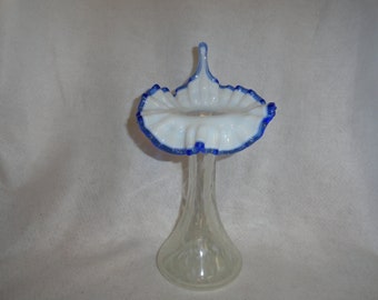 May include: A white milk glass vase with a blue rim and a ruffled top. The vase has a clear glass stem.