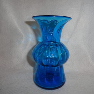 May include: A vibrant blue glass vase with a bulbous midsection and flared top. The vase has a textured, ribbed design and a glossy finish. This decorative piece is suitable for displaying flowers or as a standalone accent.