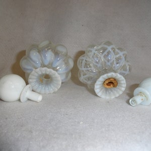 May include: Two opalescent glass perfume bottles with matching round white stoppers. One bottle features a ribbed design, while the other has a white lattice pattern. Both bottles have fluted necks and one contains a cork insert.