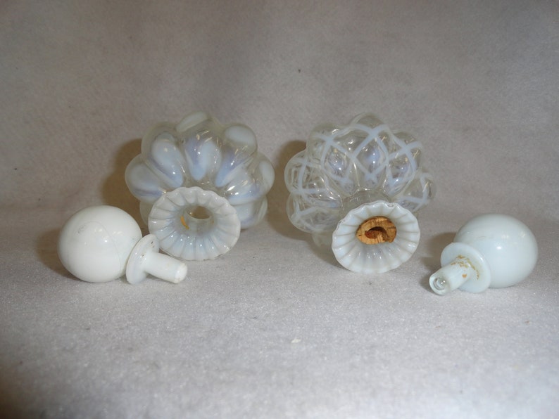 May include: Two opalescent glass perfume bottles with matching round white stoppers. One bottle features a ribbed design, while the other has a white lattice pattern. Both bottles have fluted necks and one contains a cork insert.