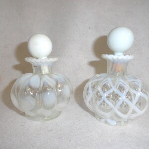May include: Two clear glass perfume bottles with opalescent white glass accents. The left bottle features a polka dot pattern, while the right bottle has a lattice design. Both bottles have ruffled necks and round, solid white glass stoppers.