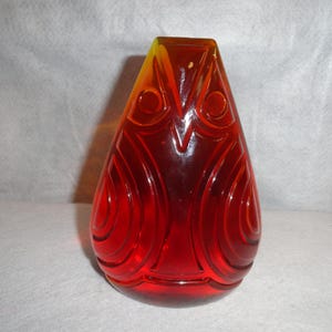 May include: A red and yellow glass owl figurine with a textured surface. The owl has large, round eyes and a beak.
