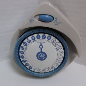Può includere: Un timer meccanico GE grigio chiaro e blu con un quadrante circolare. Il quadrante mostra i numeri da 1 a 12, AM e PM, e ha un bordo blu. Il timer ha un pulsante con l'etichetta "TIMER ON" e "OUTLET ON".