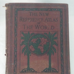 Puede incluir: Un libro antiguo titulado "The New Reference Atlas of The World". La portada es de un marrón rojizo descolorido con elementos decorativos verdes y negros. El título está en letras grandes y en negrita, y un gráfico de globo terráqueo está centrado en la portada.