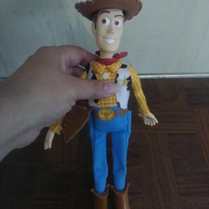 K&ouml;nnte beinhalten: Woody-Actionfigur mit braunem Cowboyhut, gelbem Hemd mit schwarzen Punkten, wei&szlig;er Weste mit Sheriffstern, blauer Hose und braunen Stiefeln. Die Figur hat ein l&auml;chelndes Gesicht und ein rotes Halstuch.