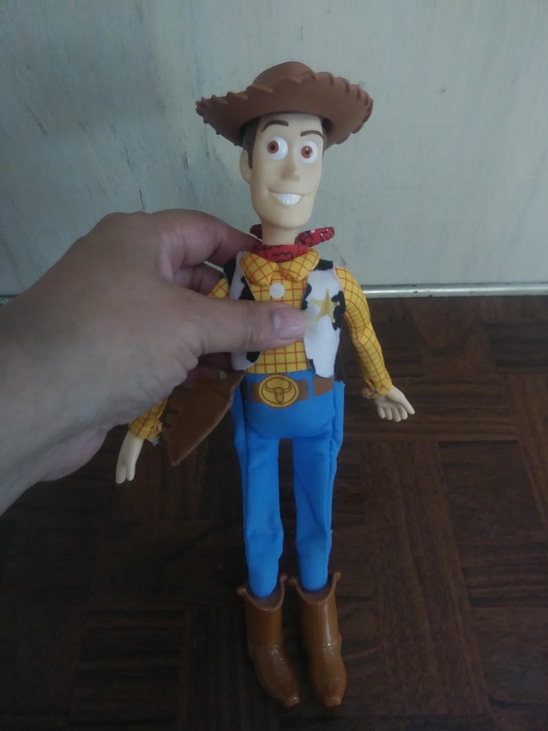 K&ouml;nnte beinhalten: Woody-Actionfigur mit braunem Cowboyhut, gelbem Hemd mit schwarzen Punkten, wei&szlig;er Weste mit Sheriffstern, blauer Hose und braunen Stiefeln. Die Figur hat ein l&auml;chelndes Gesicht und ein rotes Halstuch.