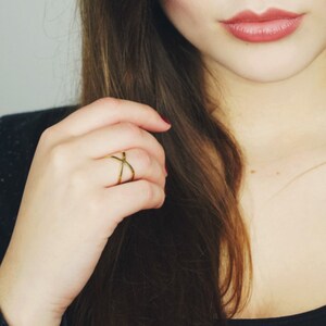 Könnte beinhalten: Ein goldener Ring mit einem Kreuz-Design. Der Ring wird am Zeigefinger einer Hand getragen.