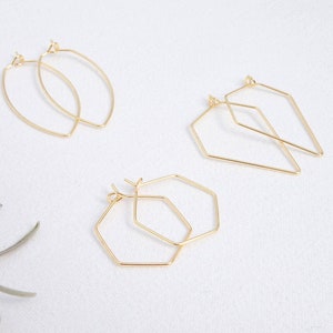 Könnte beinhalten: Drei Paar goldene Creolen mit verschiedenen geometrischen Formen. Das erste Paar ist oval geformt, das zweite Paar ist rautenförmig und das dritte Paar ist sechseckig.