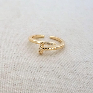 Peut inclure: Une bague dorée en forme de clou, avec une tête ornée de petits pierres précieuses transparentes. La bague est ouverte à l'arrière pour être ajustable. Le design en forme de clou est un bijou unique et moderne.