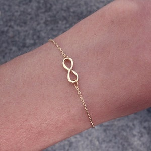Könnte beinhalten: Ein goldfarbenes Armband mit einem Unendlichkeits-Anhänger an einer Kette.
