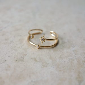 Puede incluir: Un anillo ajustable de oro con tres pequeños acentos en forma de estrella engastados con piedras de circonita cúbica transparentes.