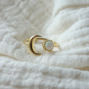 Può includere: Un anello d'oro con un design a forma di luna crescente e una pietra di opale bianca.