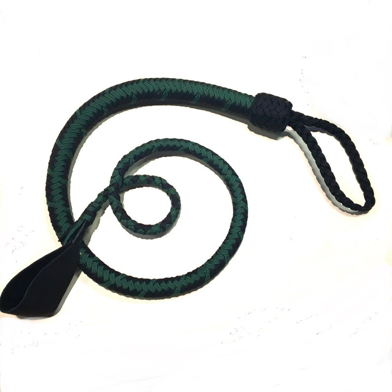May include: A braided whip with a black handle and a green and black braided body. The whip is coiled and has a loop at the end. The handle is made of a smooth, black material.