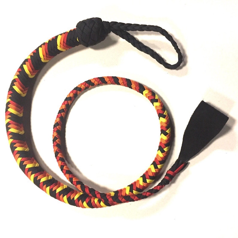 May include: A braided whip with a black handle and a long, flexible body. The body is woven with black, yellow, and red strands. The whip has a loop at the top and a flat, black end.