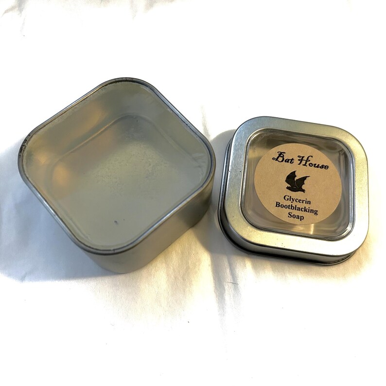 May include: A silver tin with a clear lid containing a bar of glycerin soap. The label on the soap reads "Bat House Glycerin Bootblacking Soap".