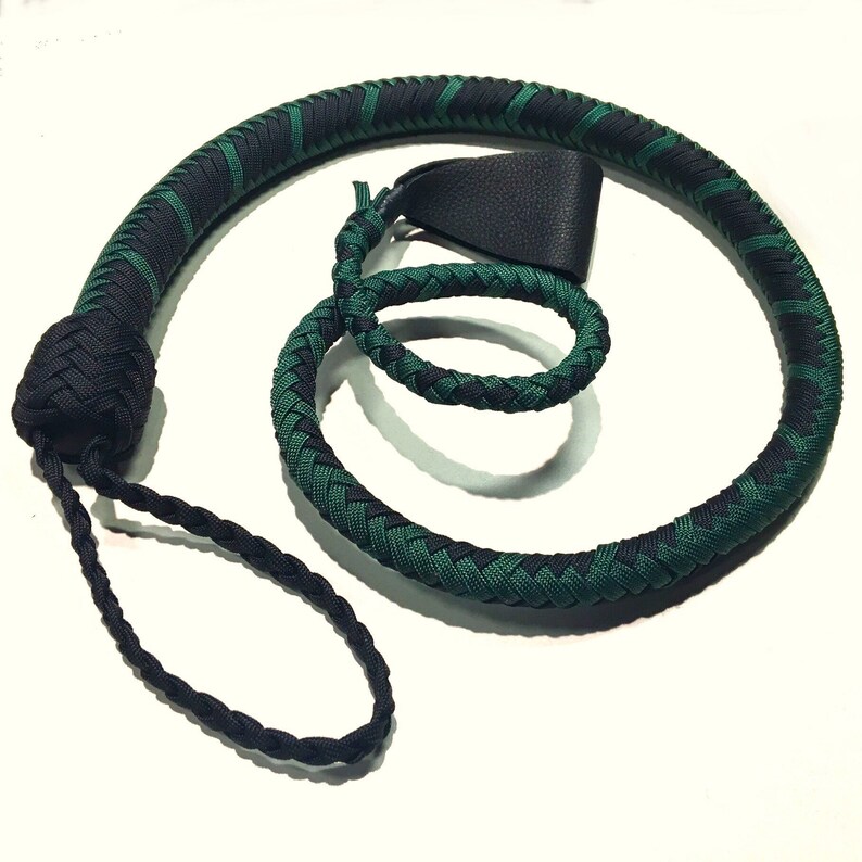 May include: A braided whip in a spiral shape, featuring alternating bands of black and dark green. The handle is black, and a black loop hangs from the base. A black leather piece is attached near the top.